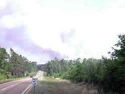 Rosalee Fire smoke rising in the background to the right of a highway.