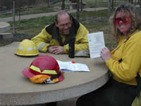 Picture of two firefighters sitting at a table, one holding up the taskbook of the other.