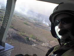 Picture of Lead Fire Effects Monitor Mindy Wright looking out of a helicopter in flight with the prescribed fire burning on the ground in the background.