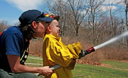 Firefighter with young boy using a fire hose.