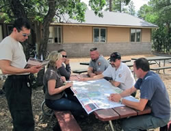 Six people in discussion at a picnic table looking over a map.