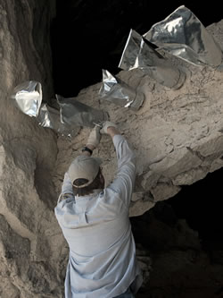 NPS staff placing protective foil caps on prehistoric wood components of a cliff dwelling.