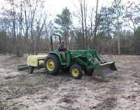 A man on a green tractor with a broadcast seeding attachment seeding an area for wildlife habitat improvement.